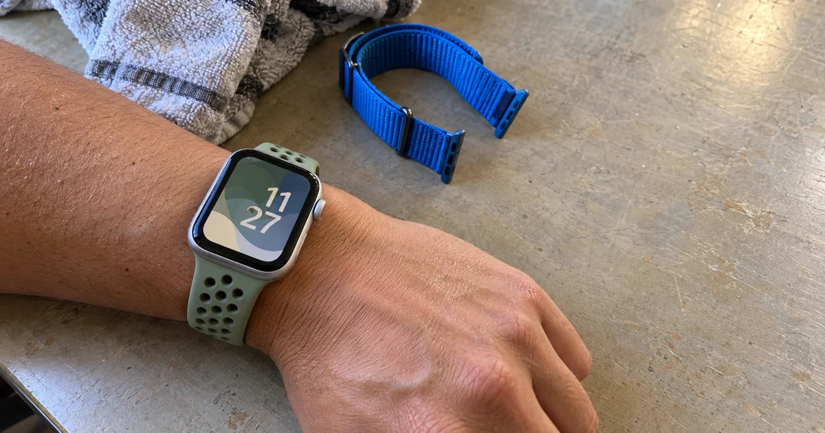 Apple Watch SE 3 avec un bracelet silicone pastel, poignet posé sur une table de café près d'un téléphone