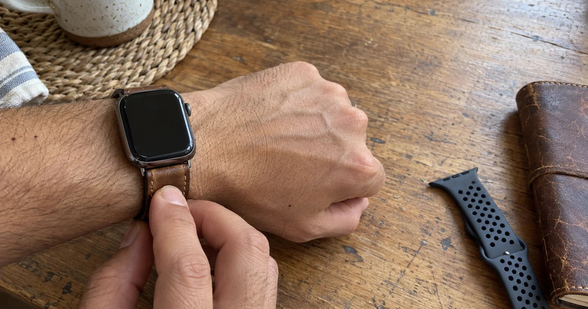 Apple Watch με καφέ δερμάτινο λουράκι ρολογιού με εμφανείς ραφές, καρπός πάνω σε ξύλινο τραπέζι