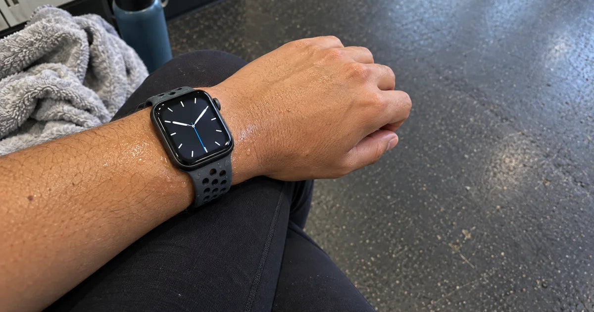 Apple Watch avec un bracelet sport perforé sur un poignet légèrement humide après l'entraînement, serviette à côté Image
