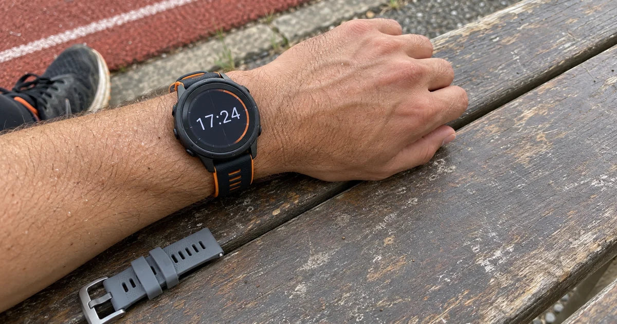 Garmin Forerunner 265 avec un bracelet silicone noir et orange sur une piste urbaine au crépuscule Slika