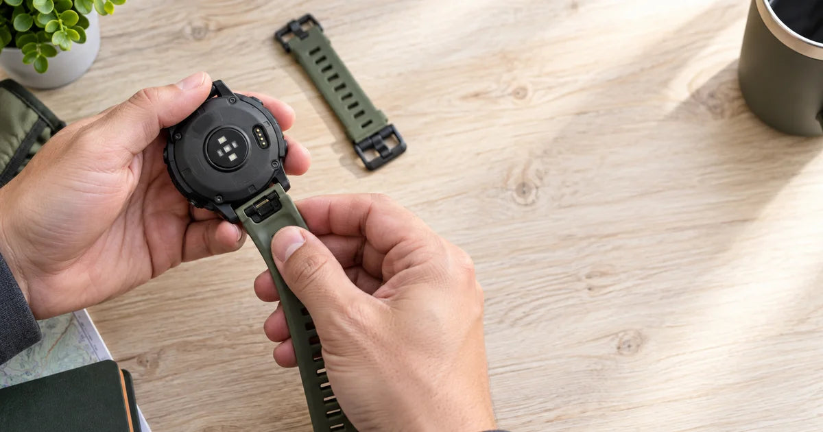 Garmin Fenix avec un bracelet nylon kaki QuickFit, doigt appuyant sur le levier de fixation sur un bureau Image